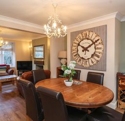 A dining area with a wooden table and six chairs next to a living room with sofas and a television at Enfield Porlock