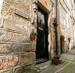 A stone building with a black door and a sign saying Inglennook on the wall at Inglenook Cottage in Whitby