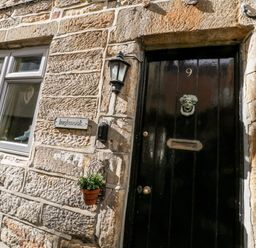 A black front door with the number 9 and a metal door knocker on a stone wall next to a window and a small plant at Inglenook Cottage in Whitby