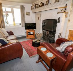 A living room with leather sofas a television a fireplace and a red rug at Inglenook Cottage in Whitby