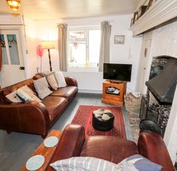 A living room with leather sofas a television a fireplace and a red rug at Inglenook Cottage in Whitby