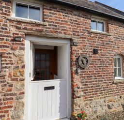 A brick building facade with a half white door and windows at The Bothy Lowick near Holy Island