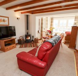 A living room with a red leather sofa a wood burning stove a television and a dining area with a round table at The Bothy in Lowick near Holy Island
