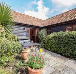 A patio with potted plants a bench and a table outside a building with tiled roof at Poppy Cottage in Little Glemham near Wickham Market