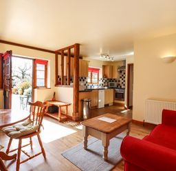 A living room and kitchen with wooden furniture and red sofa at Poppy Cottage in Little Glemham near Wickham Market