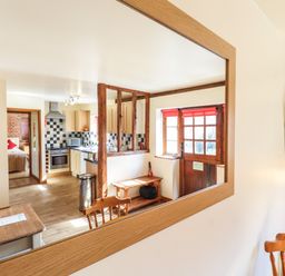 A reflection of a kitchen and entrance door with wooden bench and a dining table with chairs at Poppy Cottage in Little Glemham near Wickham Market