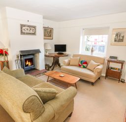 A living room with a green sofa, a beige sofa, a wooden coffee table, a fireplace, a small TV on a round wooden table, and framed pictures on white walls at 28 Oxborough in Oxborough