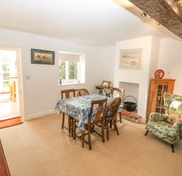 A dining room with a wooden table covered by a blue and white tablecloth surrounded by wooden chairs near a window and an armchair at 28 Oxborough in Oxborough