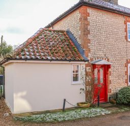 The exterior of a stone and brick house with a red door and tiled roof at 28 Oxborough in Oxborough