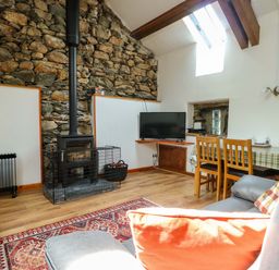 A living room with a wood stove, television, and dining table at Bythyn Ddol Hafod, Capel Curig