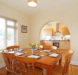 A dining room with a wooden table and chairs next to a window and an archway leading to a kitchen at Trysor Y Mor in Borth