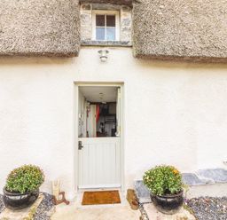 An entrance with a white half-door flanked by two potted plants under a thatched roof at New Thatch Farm Scarteen near Knocklong County Limerick