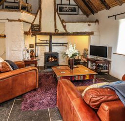A living room with two leather armchairs a coffee table a wood burning stove and a television at New Thatch Farm Scarteen near Knocklong County Limerick