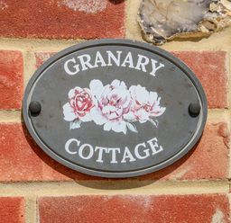 An oval sign reading Granary Cottage with flowers on a brick and stone wall at The Granary Cottage in Gayton near King's Lynn