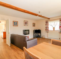 A living room with brown leather sofas a wooden dining table a television and floral curtains at The Granary Cottage in Gayton near Kings Lynn