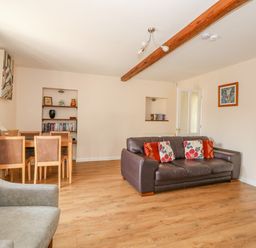 A living room with a brown leather sofa, armchair, dining table with chairs, wooden floor and bookshelves at The Granary Cottage in Gayton near King's Lynn