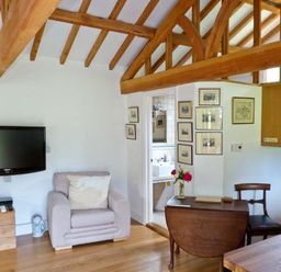 A room with wooden beams a beige armchair a wall-mounted television a small wooden table with flowers and a wooden chair at The Springs in Ashey near Brading and Ryde