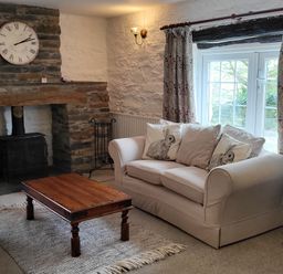 A living room with a stone fireplace a wooden coffee table and a sofa with rabbit cushions at High Kiln Bank Cottage in Seathwaite Duddon Valley