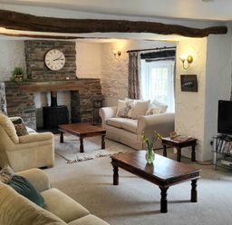 A living room with sofas a stone fireplace wooden tables a television and a vase with flowers at High Kiln Bank Cottage in Seathwaite Duddon Valley