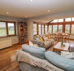 A living room with a bookshelf and large windows at Lough Cluhir Cottage in Union Hall, County Cork