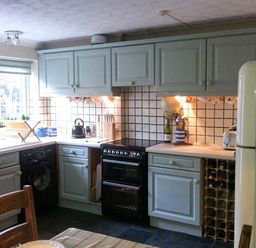 A kitchen with light blue cabinets black stove and a cream refrigerator at Teds Place in Aylsham