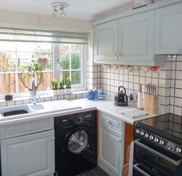 A kitchen with a sink under a window a black washing machine a stove and light blue cabinets at Teds Place in Aylsham