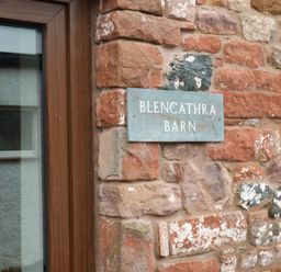 A close up of a stone wall with a metal sign reading Blencathra Barn next to a wooden framed window at Blencathra Barn in Penrith