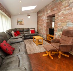 A living room with a grey leather sectional sofa and a brown reclining chair with ottoman near a stone wall with a TV at Blencathra Barn in Penrith
