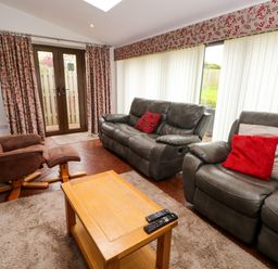 A living room with leather sofas a reclining chair coffee table and large windows with curtains at Blencathra Barn in Penrith