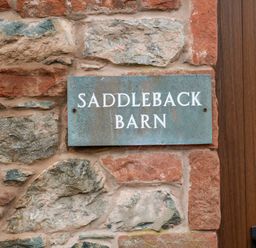 A sign reading Saddleback Barn on a stone wall next to a wooden door at Saddleback Barn in Newton Reigny near Penrith