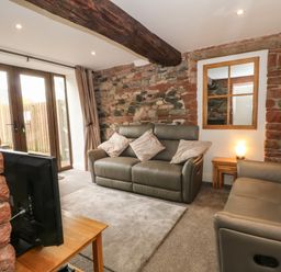 A living room with two grey sofas a television on a wooden stand and a mirror on a stone wall at Saddleback Barn in Newton Reigny near Penrith