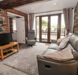 A living room with a sofa and armchair facing a television on a wooden stand at Saddleback Barn in Newton Reigny near Penrith