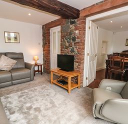 A living room with grey sofas a TV on a wooden stand and a doorway leading to a dining area at Saddleback Barn in Newton Reigny near Penrith