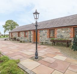 An outdoor view of a stone cottage with a tiled walkway and lamp posts at Lily Cottage in Caeathro near Caernarfon