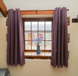 A window with curtains and flowers on the sill at Lavender Cottage in Caeathro near Caernarfon