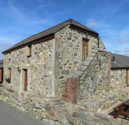 A stone building with a staircase and outdoor seating at Bluebell Cottage in Caeathro near Caernarfon