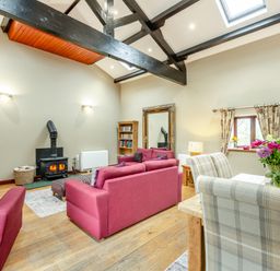 A living room with pink sofas a wood stove a dining table with plaid chairs and flowers at Hill Side Barn in Pennington near Ulverston