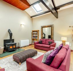 A living room with two red sofas a striped ottoman a wood burning stove bookshelf and a large mirror at Hill Side Barn in Pennington near Ulverston
