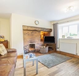 A living room with a leather sofa and coffee table by a fireplace with a TV and window at Ty Nant in Betws-y-Coed