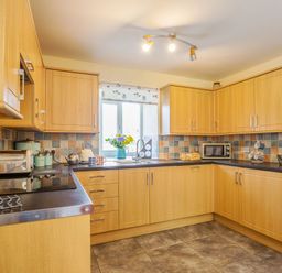 A kitchen with wooden cabinets a toaster a microwave a fruit basket and flowers on the counter at Ty Nant in Betws-y-Coed