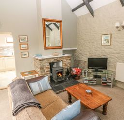 A living room with a wood burning stove a sofa and a wooden coffee table at Foxglove Cottage in Little Haven near Haverfordwest