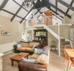 A living room with sofas a wooden coffee table a staircase leading to a loft and a dining table with chairs at Foxglove Cottage in Little Haven near Haverfordwest