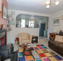 A living room with a leather sofa armchair colorful rug fireplace and a view into the kitchen at Peggottys Kelsale near Saxmundham