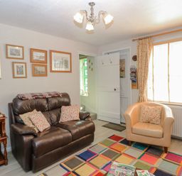 A living room with a brown leather sofa and a beige armchair near a window with curtains at Peggotty's in Kelsale near Saxmundham