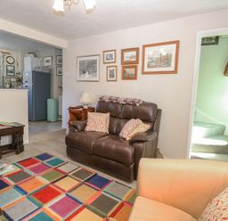 A living room with leather sofas colorful rug and kitchen area in the background at Peggotty's Kelsale near Saxmundham