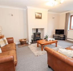 A living room with leather sofas wooden coffee table wood stove and television at Bryn Seion in Y Felinheli