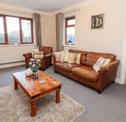 A living room with brown leather sofa and armchair wooden coffee table with vase and teapot at Bryn Seion in Y Felinheli