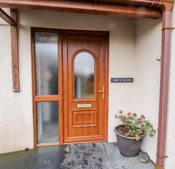 A wooden front door with frosted glass panels a flower pot with plants and a sign reading Bryn Seion at Y Felinheli