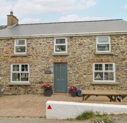 Stone house with blue door and windows with flower pots and wooden bench at Hillbrook House in Nolton Haven