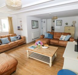 A living room with two brown leather sofas a wooden coffee table with flowers and books a television on a white console and framed pictures on the walls at Hillbrook House in Nolton Haven